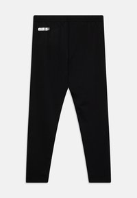 Črne oprijete pajkice z elastičnim pasom in majhnim srebrnim logotipom "KOMBAT" na zgornji levi strani.