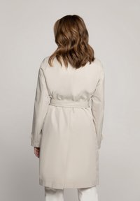 Beige trenchcoat met een ceintuur in de taille, lange mouwen en een gladde, matte afwerking. Heeft een rugventilatie voor gemakkelijke beweging.