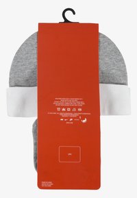 Beanie grigio e bianco con risvolto, attaccato a un'etichetta di cartone rossa che mostra istruzioni per la cura e dettagli del marchio.