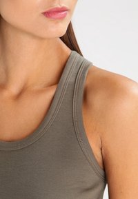 Top de tanque color caqui con un escote redondo y tirantes anchos. Tejido suave y elástico con un ligero acanalado para darle textura. Diseño ajustado.