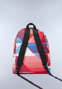 Mochila con patrón geométrico en rojo, azul y blanco. Cuenta con correas ajustables negras y un asa para un transporte fácil.