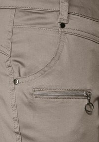 Gråbyxor med grov textur, med en framficka och en extra ficka med dragkedja och silverfärgad hårdvara.