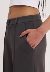 Gray tailored trousers with a smooth texture, front pleats, side pockets, and a single black button closure at the waist.