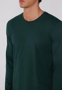 T-shirt z długim rękawem w ciemnozielonym kolorze, okrągły dekolt, gładka tekstura, dopasowany krój, minimalne detale.