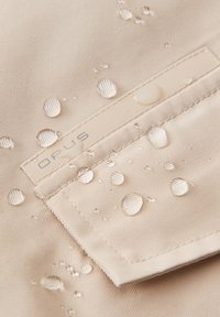 Tessuto beige resistente all'acqua con gocce d'acqua. Presenta un'etichetta cucita con la scritta "OPUS" e un motivo di superficie testurizzato.