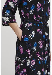 Svart blommig klänning med mönster av lila, blå och vita blommor, knappp detaljer och midja med bälte. Inkluderar sidofickor och trekvartsärmar.