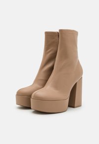 Ett par beige plattform ankelstövlar med kraftiga klackar och sidodragkedjor, visade på en vit bakgrund.