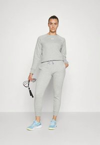 Sweat-shirt gris et pantalon de jogging en matériau doux, coupe ajustée, taille élastique. Personne tenant une corde à sauter, portant des chaussures de sport bleues.