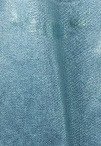 Tissu en denim bleu clair avec texture de tissage diagonal visible et plis subtils.