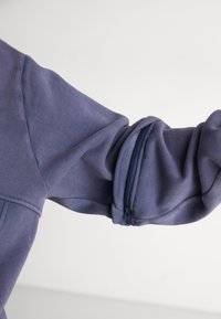 Myk, teksturert blå sweatshirterm med glidelås ved mansjetten for justerbar passform, med en glatt, strømlinjeformet design.
