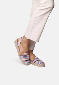 Sandali espadrillas a righe con suola in juta, dotati di una parte superiore in tessuto multicolore e cinture color cammello che si incrociano sopra il piede.