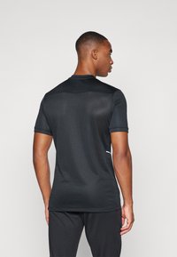 T-shirt de sport noir à manches courtes, fabriqué en tissu léger. Présente un design texturé et un accent blanc sur le côté.