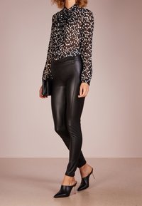 Black and white polka dot blouse with long sleeves and a bow tie detail, paired with tight-fitting black faux leather pants and black mules.