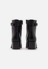 Botines negros hasta el tobillo con cuero texturizado, punta cuadrada ligeramente afilada y tacón cuadrado. Presentan cremalleras laterales y correas ajustables.