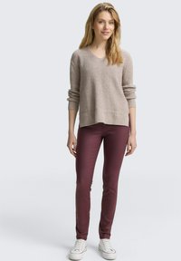 Pull en tricot beige à côtes avec décolleté en V et manches retroussées, associé à un pantalon slim bordeaux et des baskets blanches.
