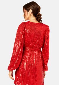 Red sequin dress with long sleeves and a cinched waist. The fabric has a shiny, textured surface with a belt accent at the waist.