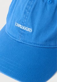 Μπλε καπέλο μπέιζμπολ με λευκή κεντημένη λέξη "UNPLUGGED" στον μπροστινό πίνακα.