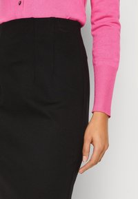 Getailleerde zwarte kokerrok met voorste plooien, gecombineerd met een levendig roze gebreid top met lange mouwen, met ribbelmanchetten en een soepele textuur.