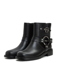 Botine negre până la gleznă, confecționate din piele netedă, având două curele reglabile cu catarame și un accent metalic circular pe lateral. Talpă plată.
