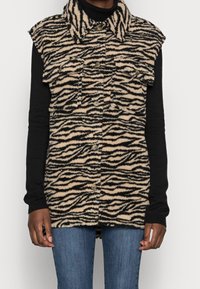 Fuzzy, beige och svart zebramönstrad väst med krage, tryckknappar och frampocketar. Bärs över en svart långärmad topp.