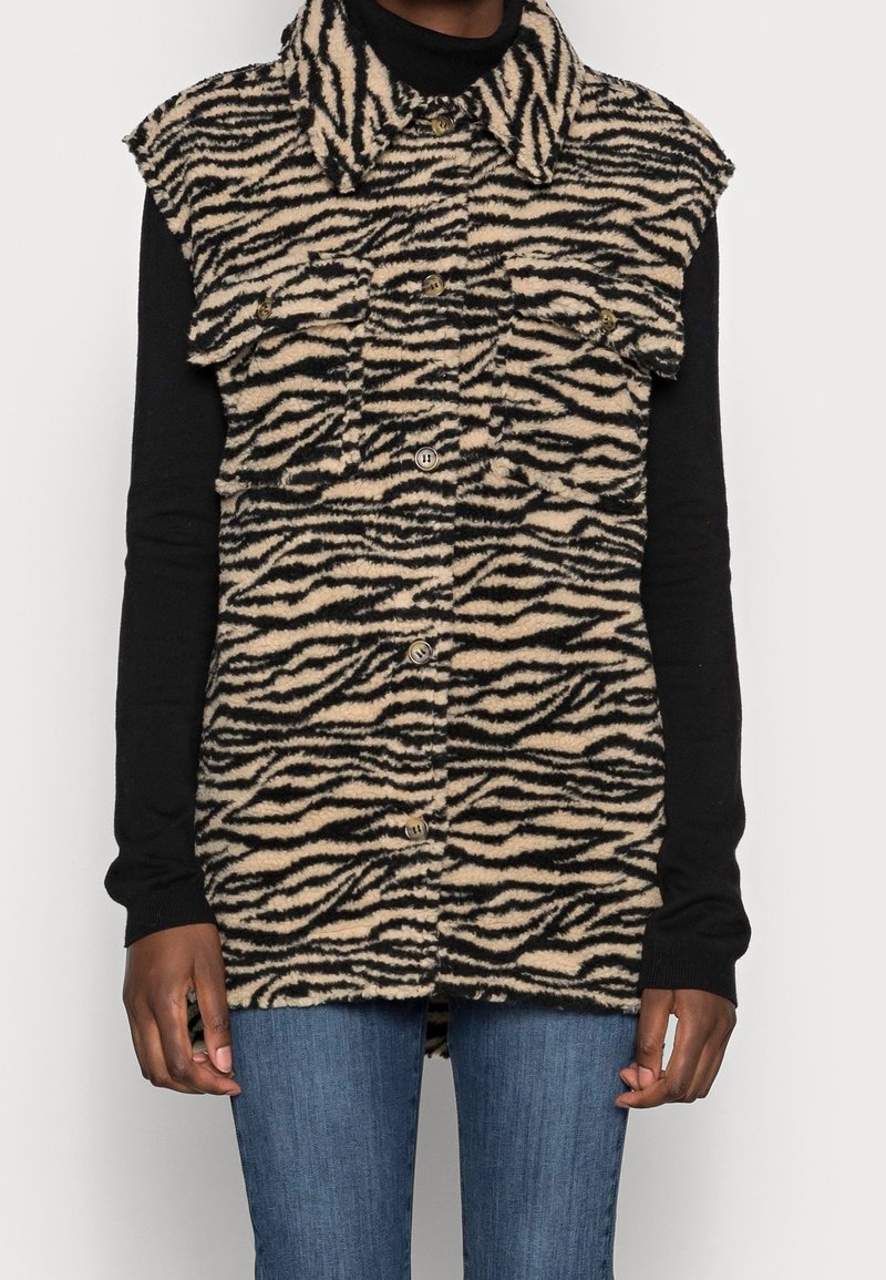 Fuzzy, beige och svart zebramönstrad väst med krage, tryckknappar och frampocketar. Bärs över en svart långärmad topp.