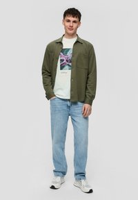 Groene overhemd met knopen over een witte graphic t-shirt, gecombineerd met lichtblauwe jeans en witte sneakers. Soepele stof en een ontspannen pasvorm.
