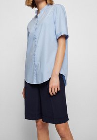 Hellblaues kurzärmeliges Hemd mit Kragen, das eine lockere Passform und eine glatte Textur aufweist, kombiniert mit dunkelblauen knie-langen Shorts.