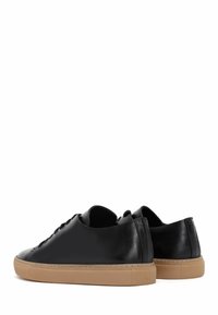 Sneaker nere in pelle con una texture liscia, punta rotonda, taglio basso e suola in gomma naturale. Presentano lacci piatti e cuciture minime.