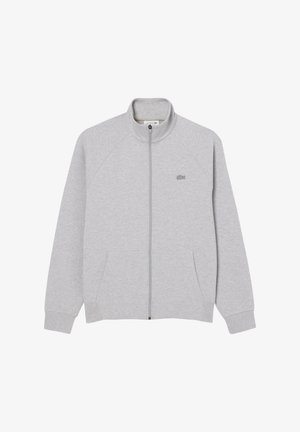 Veste zippée grise en tissu doux, avec des manches raglan, un col haut et deux poches avant. Logo Lacoste sur la poitrine gauche.