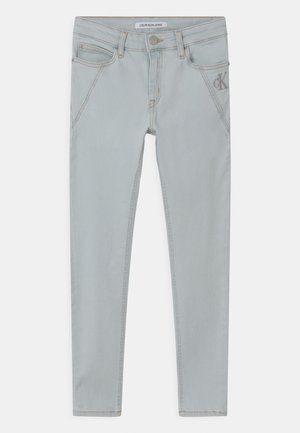 Jean slim gris clair avec poches avant, fermeture à boutons et petit logo "CK" sur la poche droite.