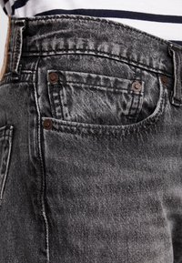 Jeans en denim noir avec un design classique à cinq poches, légère décoloration, quincaillerie en métal et détails de coutures visibles.