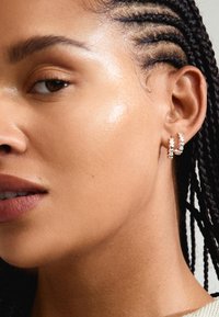 Orecchini a cerchio in argento con un design testurizzato e intrecciato, su uno sfondo di una prima persona con pelle morbida e naturale e capelli intrecciati.