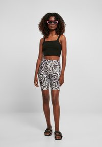 Juodas trumpas tank top'as ir zebra rašto dviratininkų šortai, papildyti rožiniais akinių nuo saulės ir juodais sandalais. Lygus audinys, prigludusi forma.