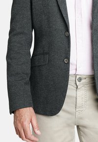 Blazer gris oscuro texturizado con un diseño de un solo botón, cierre de dos botones y un bolsillo en el pecho; combinado con pantalones beige claros.