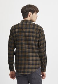 Camisa de cuadros marrón y negra en un tejido suave, con cuello abotonado, mangas largas y dobladillo redondeado, con botones negros en los puños.