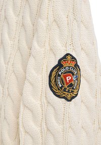 Cremfarbener Kabelstrickpullover mit einem auffälligen gestickten Polo Club-Logo in Schwarz, Gold und Rot. Der strukturierte, dicke Stoff sorgt für zusätzliche Wärme.