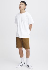 White cotton t-shirt, brown rolled hem shorts, white sneakers with black stripes, and white crew socks. Simple design with a relaxed fit.