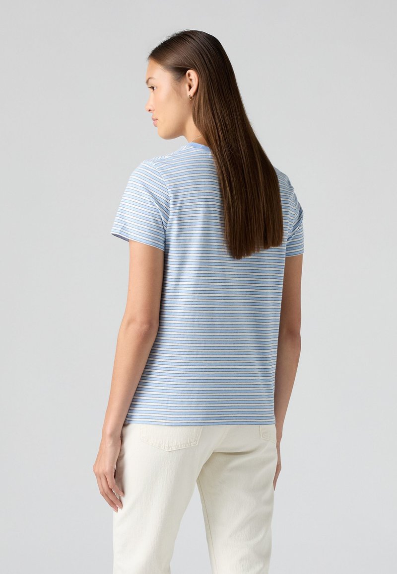 Maglietta a righe di colore azzurro chiaro con righe bianche, maniche corte, scollatura rotonda; il tessuto sembra morbido e informale. Indossata con pantaloni color crema.