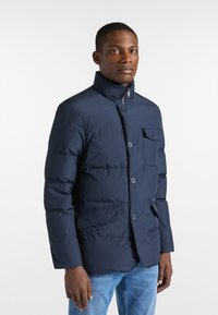 Giacca imbottita blu navy con colletto alto, chiusura a bottoni e tasca frontale, caratterizzata da una texture liscia e un design strutturato.