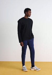 Sort langærmet skjorte parret med navy joggers, der har skrå syninger og elastiske manchetter. Båret med hvide og grå sneakers.