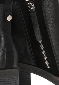 Bota negra hasta el tobillo con materiales de cuero texturizado y ante, un zipper lateral y un tacón grueso con un detallado acanalado.