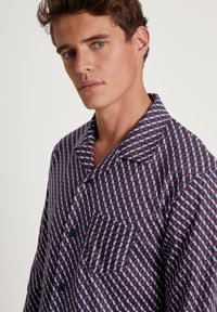 Marineblauw shirt met een geometrisch ontwerp in blauw en rood, met een kraag en een zak aan de linkerkant. Zachte stof textuur.