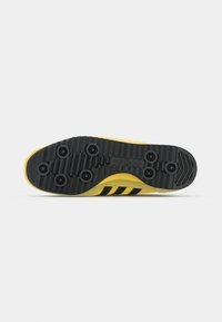 Sola de sapato Adidas com um esquema de cores amarelo e preto, apresentando uma superfície texturizada de borracha preta e três riscas pretas.