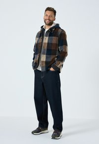 Prunditud flanellist särk pruunis, tumesinises ja koorevärvis; halli kapuutsiga särgi peale pandud. Laia lõikega tumedad teksad ja mustad ja rohelised jooksujalanõud.