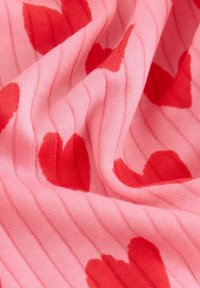 Rosa gestrickter Stoff mit roten Herzmustern auf einem gestreiften Hintergrund. Weiche Textur mit abwechselnden gerippten Abschnitten.