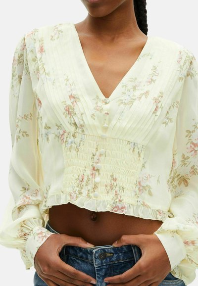 Blusa leggera gialla con motivo floreale, scollatura a V, design plissettato, vita smock e maniche lunghe, con bottoni e orlo arricciato.