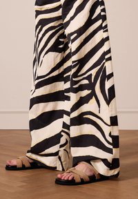 Zebra print broek in zwart-wit, gemaakt van lichte stof, met wijde benen, aangevuld met tan gekruiste sandalen met een zwarte zool.
