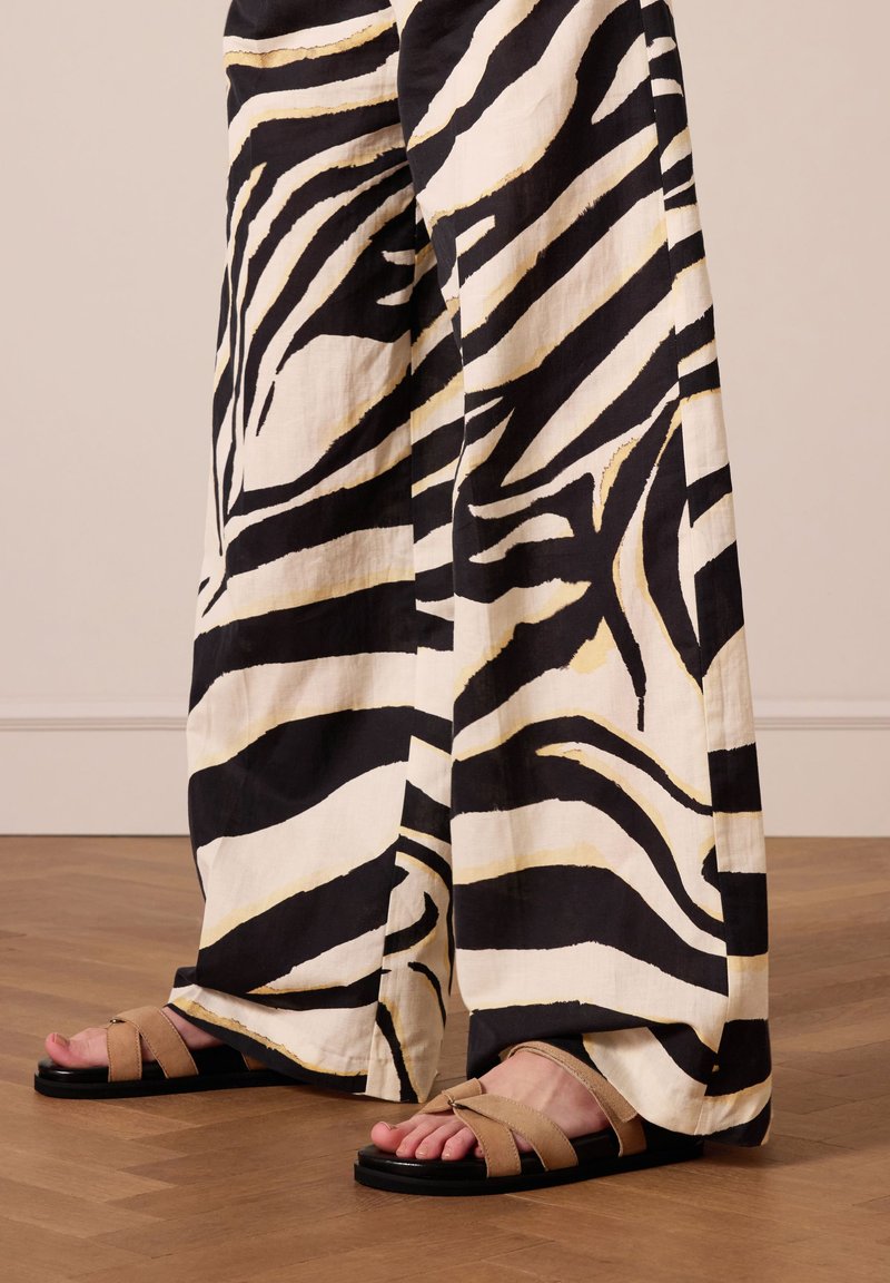 Zebra print broek in zwart-wit, gemaakt van lichte stof, met wijde benen, aangevuld met tan gekruiste sandalen met een zwarte zool.