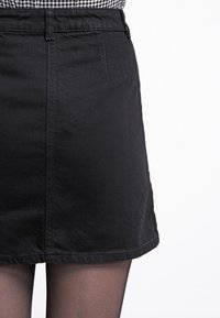 Svart denim A-linje kjol med rak fåll, med framfickor och bälteslörer. Tyget har en mjuk textur och en klassisk design.