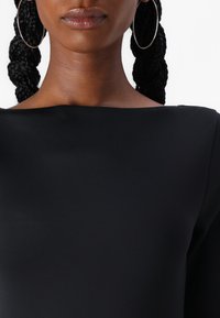 Black, smooth fabric dress with a wide neckline. Close-up view highlighting intricate braiding and large silver hoop earrings.